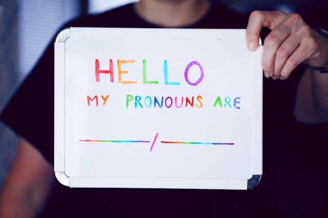 Une personne qui tient une ardoise sur laquelle est écrite : My pronouns are